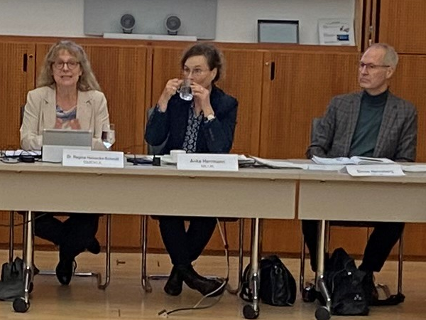 Vier Personen an einem Tisch vor einem an die Wand projizierten Vortrag.