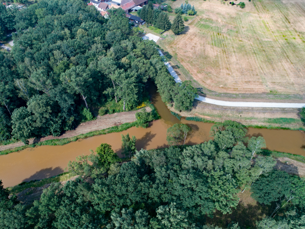 Ein Fluss mit relativ klarem Wasser mündet in einen größeren Fluss mit trübem, rötlich braunem, Wasser.